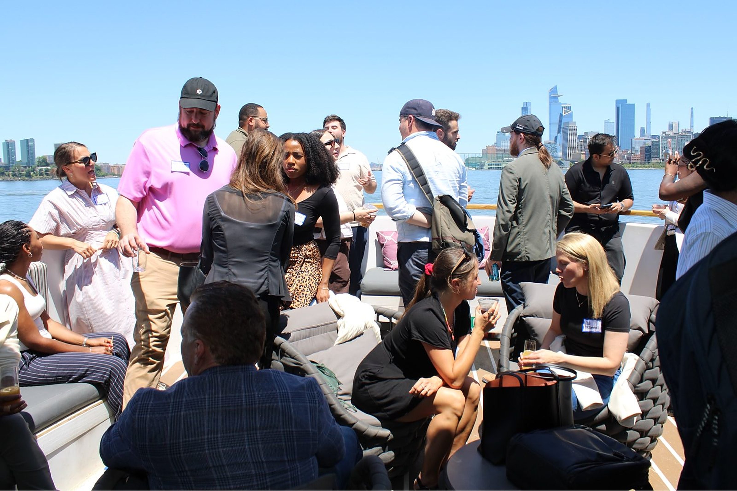 Heartland Venture Summit guests in conversation in the lounge seating on the Hornblower Lexington with the Hudson River and Manhattan skyline behind them